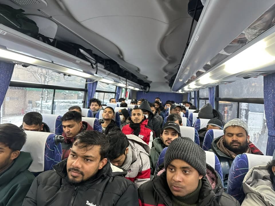 A crowded tour bus filled with men in winter coats and hats, seated in rows, with a snowy landscape visible through the windows.