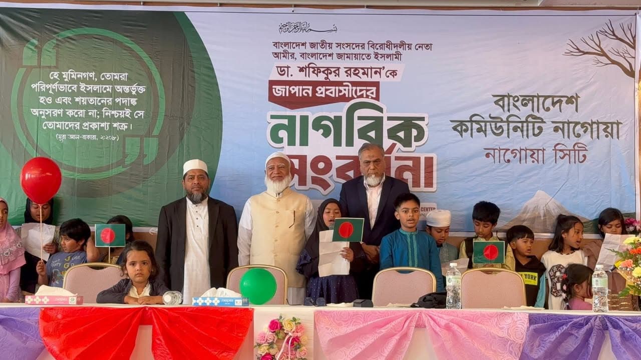 Three men in formal attire stand on a stage in front of a large banner with Bengali text, surrounded by children holding small Bangladeshi flags and a red balloon, at an event organized by the Bangladesh Community of Nagoya City.