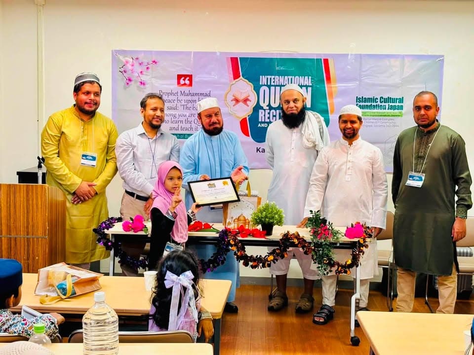 A young girl in a pink hijab stands on a table holding a certificate in a decorative frame, surrounded by six men in traditional Islamic attire, in front of a banner reading "International Qur'an Recitation" at an indoor event.