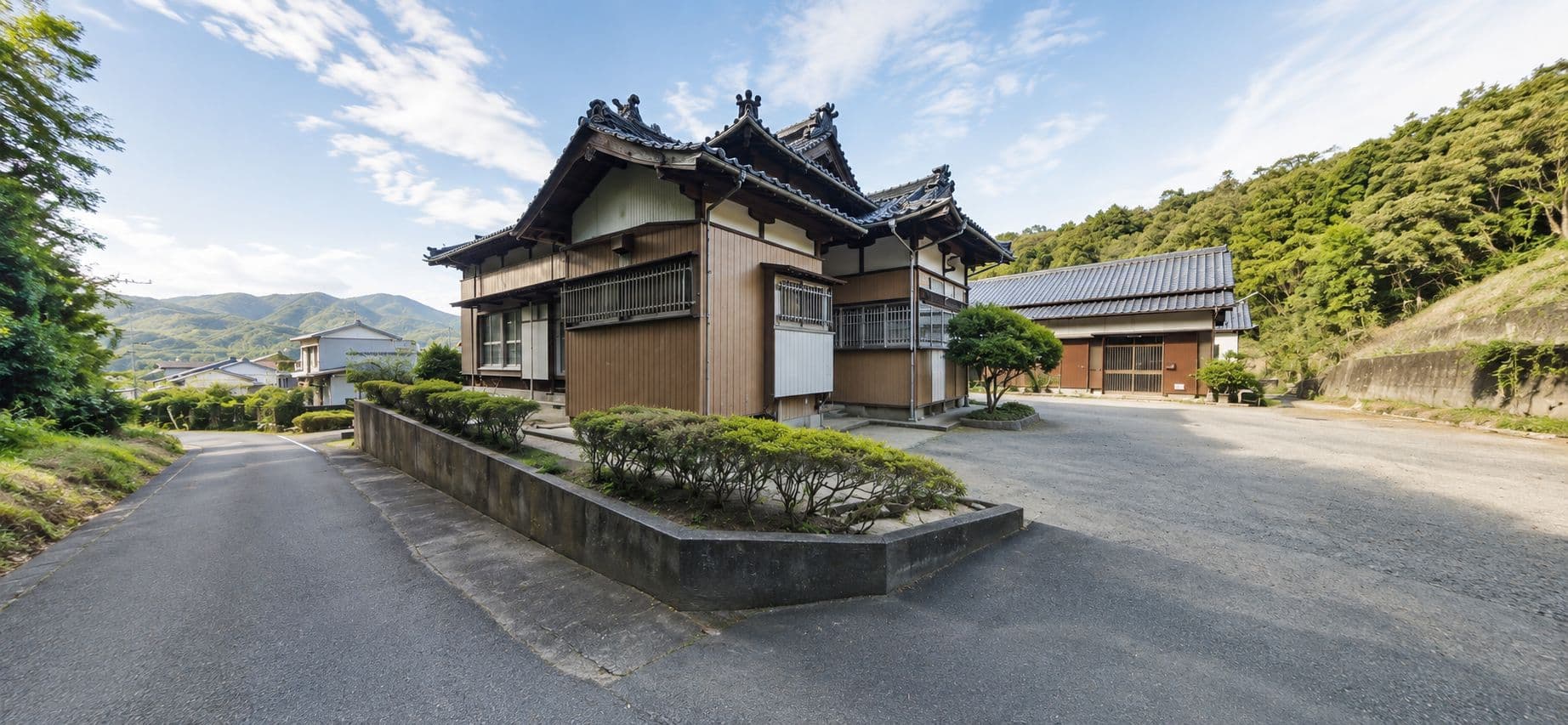 Wide view of the traditional Japanese building proposed as the Aichi Islamic Bunka Center, with a tiled roof and timber facade, a hedge and driveway in front, and wooded hills behind.