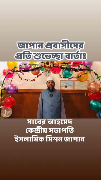 A man in a grey Islamic robe with a cap stands and speaks in front of a wall decorated with colorful balloons and floral arches, with Bengali text overlaid reading a greeting message to Japan's expatriate community and identifying him as the Central President of Islamic Mission Japan.