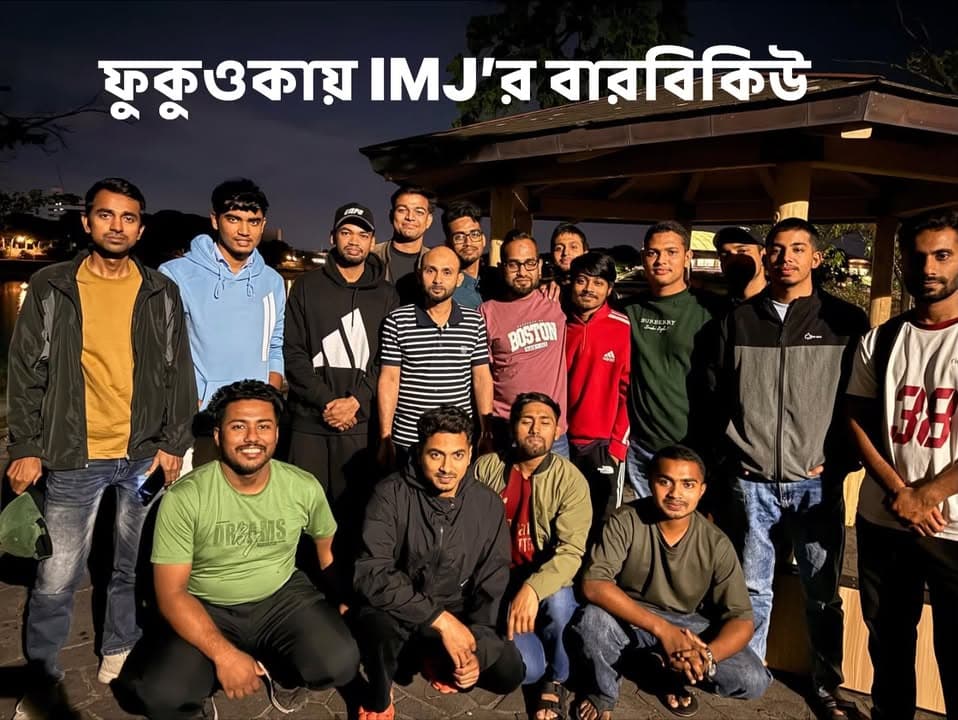 A group of about seventeen men pose together for a nighttime photo under a wooden gazebo in a park, with the Bengali text "IMJ's BBQ in Fukuoka" overlaid at the top.